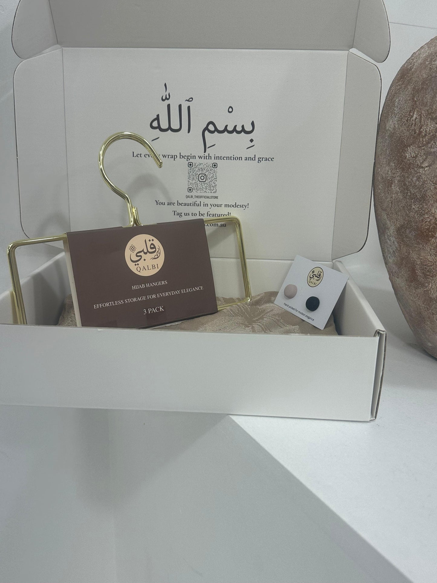 The box includes a gold hanger and carefully placed small items, set on a clean white surface.