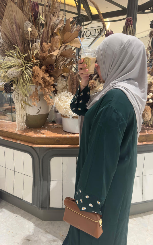 Green embroidered abaya shown in a lifestyle scene near a wooden table