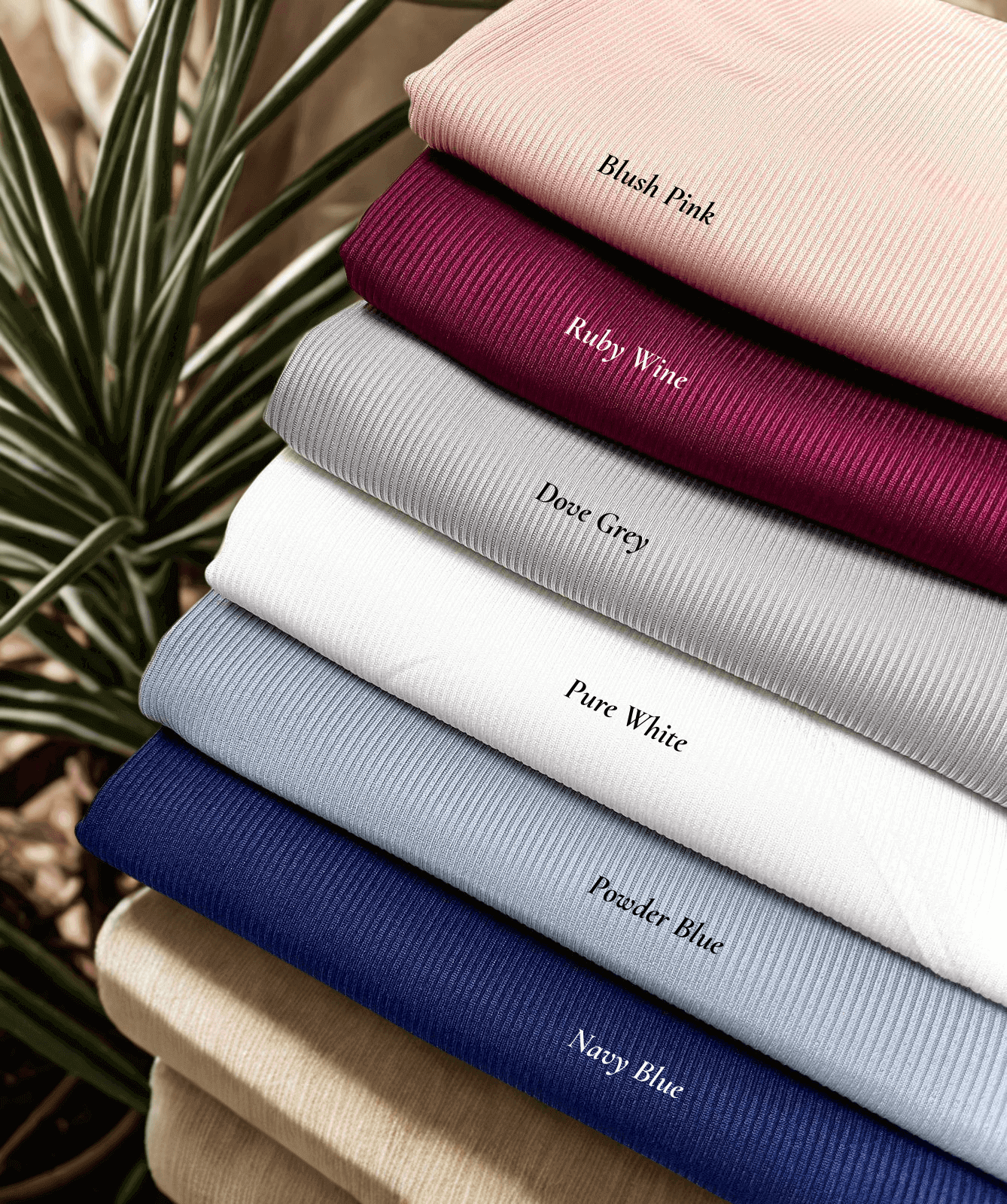 Flat lay of hijabs stacked including blush pink, ruby wine, dove grey, pure white, powder blue, navy blue textured jersey hijab – Qalbi