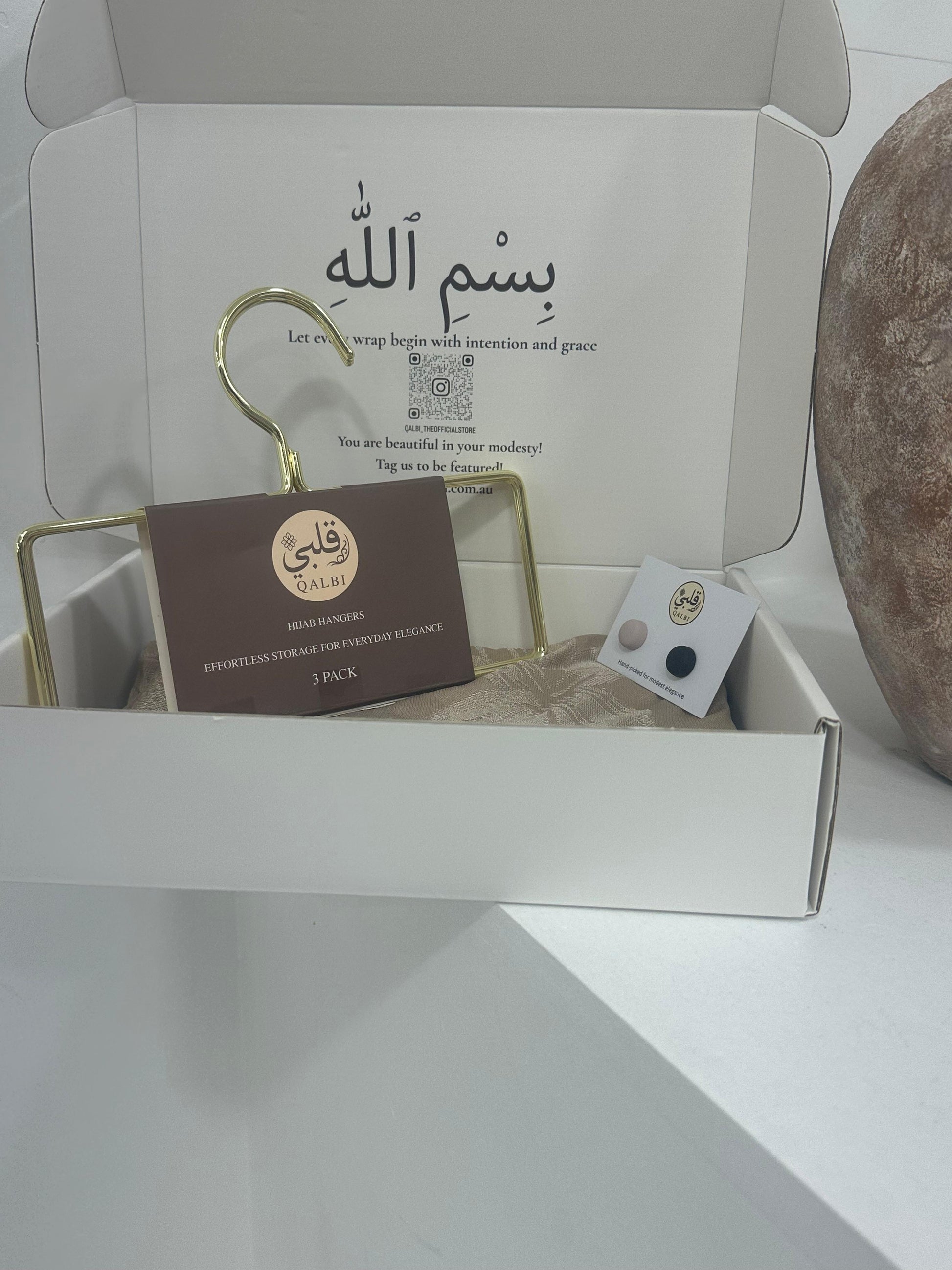 The box includes a gold hanger and carefully placed small items, set on a clean white surface.