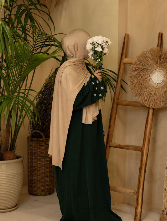 Emerald green embroidered abaya displayed in a warm indoor setup with natural décor