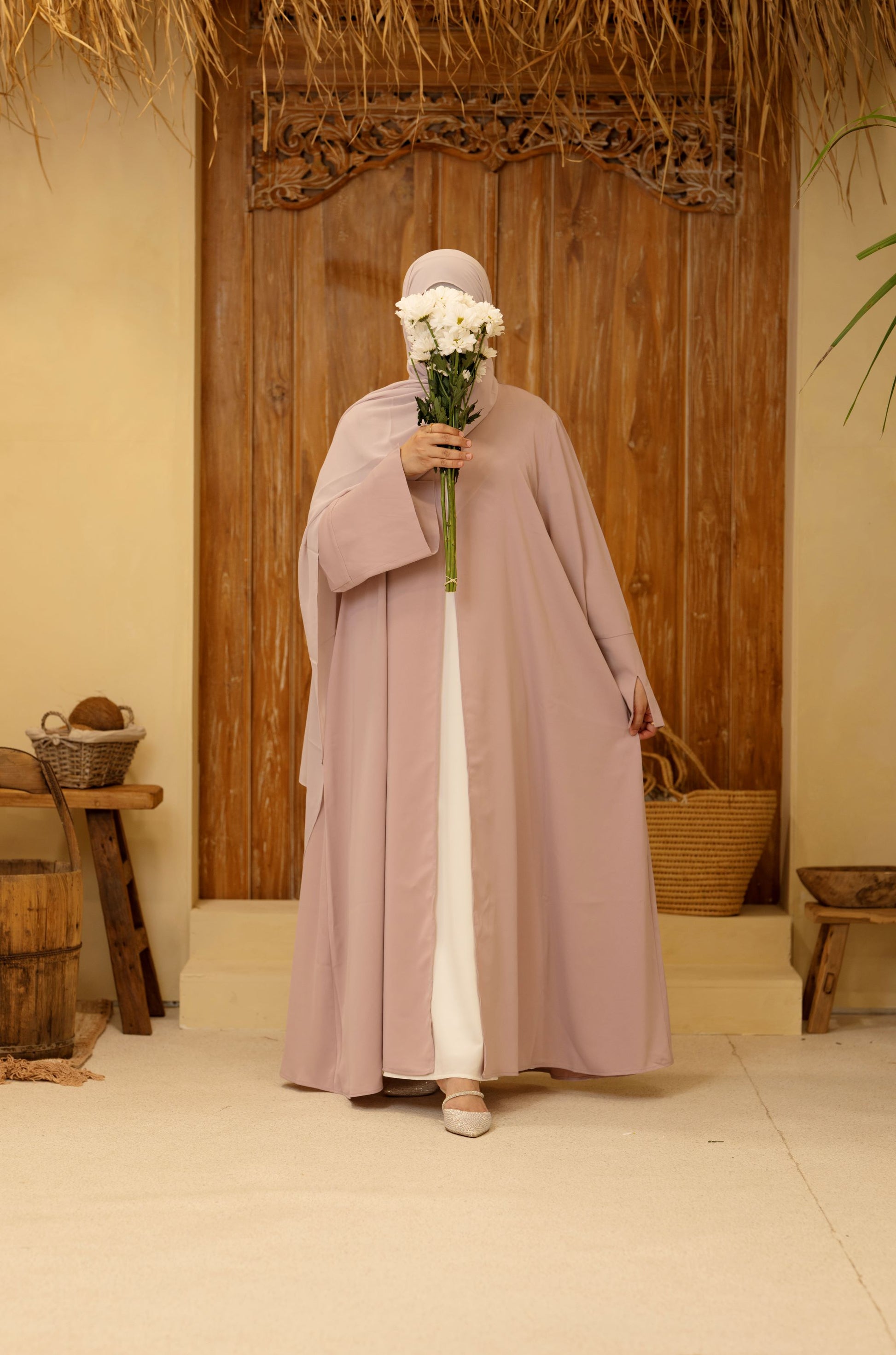 Woman wearing a rose mist Qalbi Classic Abaya holding flowers, highlighting the modest design and matching hijab.