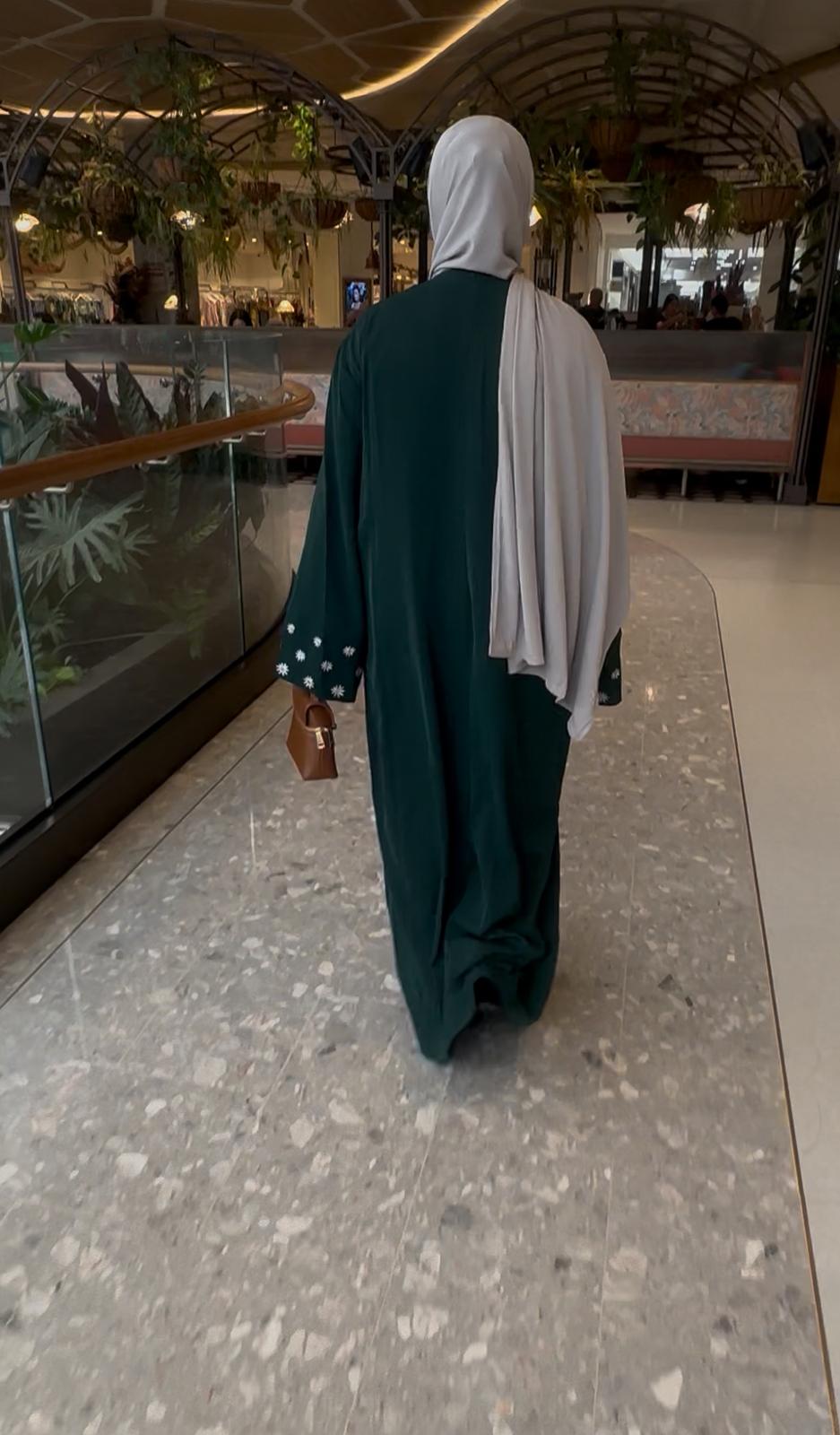 Woman wearing a dark green embroidered abaya while walking outdoors