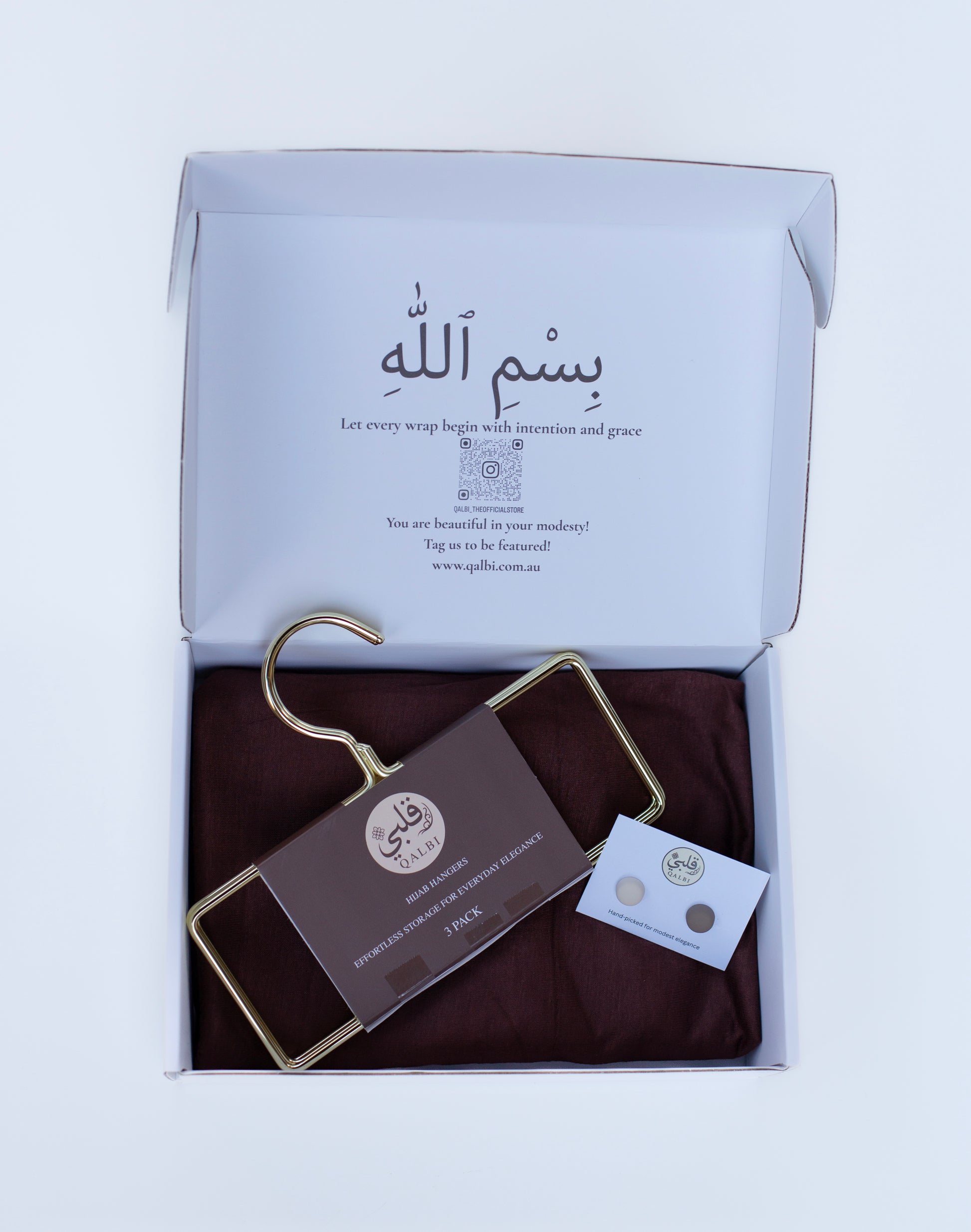 Elegant Qalbi Hijab and Accessories Gift Box unboxing. Shows the Textured Jersey Hijab, gold hangers, and magnet card set nested inside the premium white gift box.